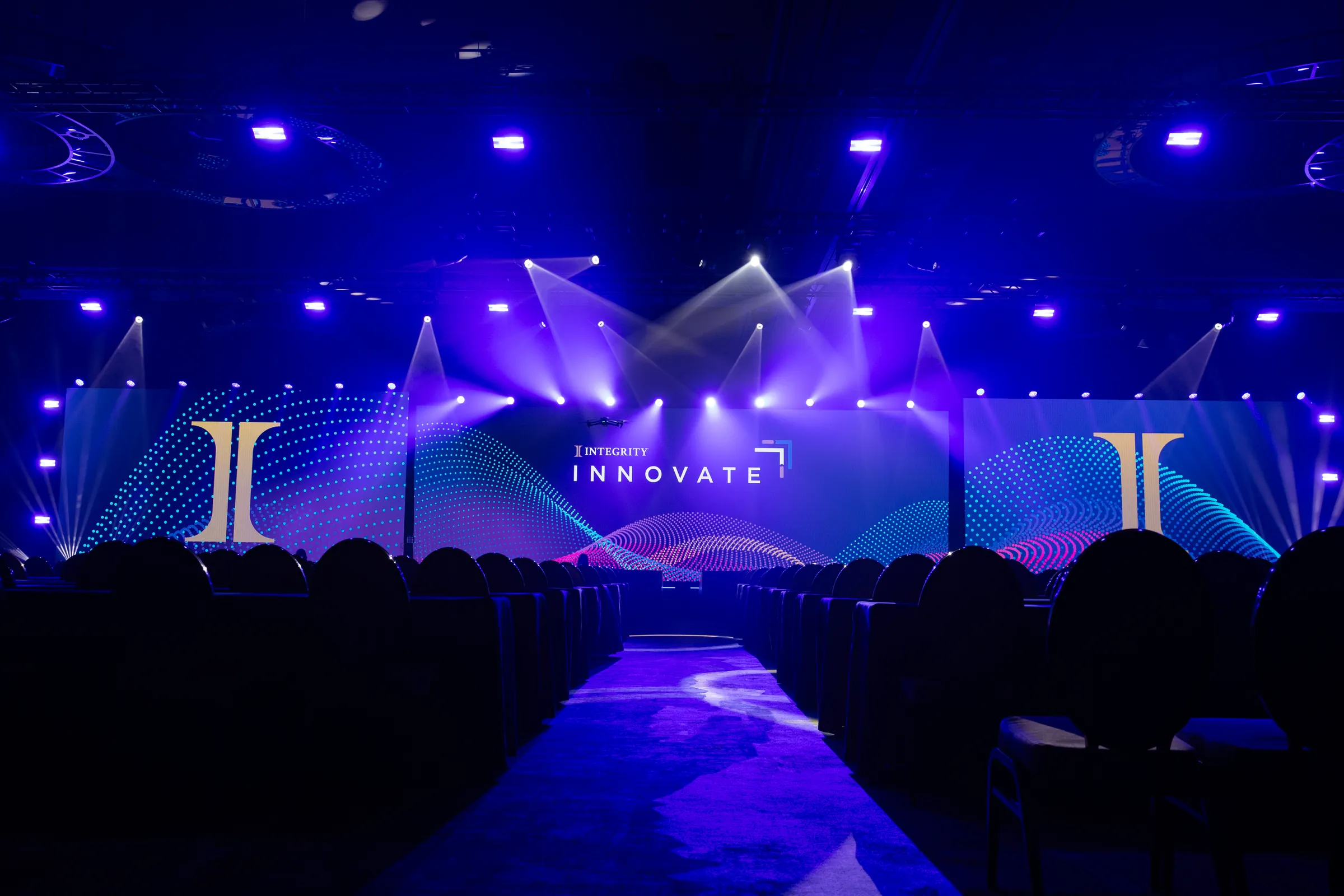Integrity Innovate general session stage with LED screens and purple lighting above rows of seats.