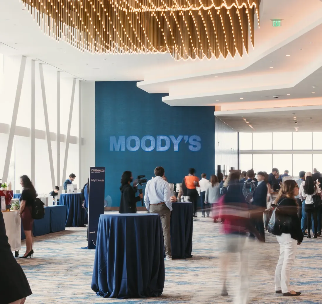 Attendees networking in the foyer beneath a large Moody’s logo wall.
