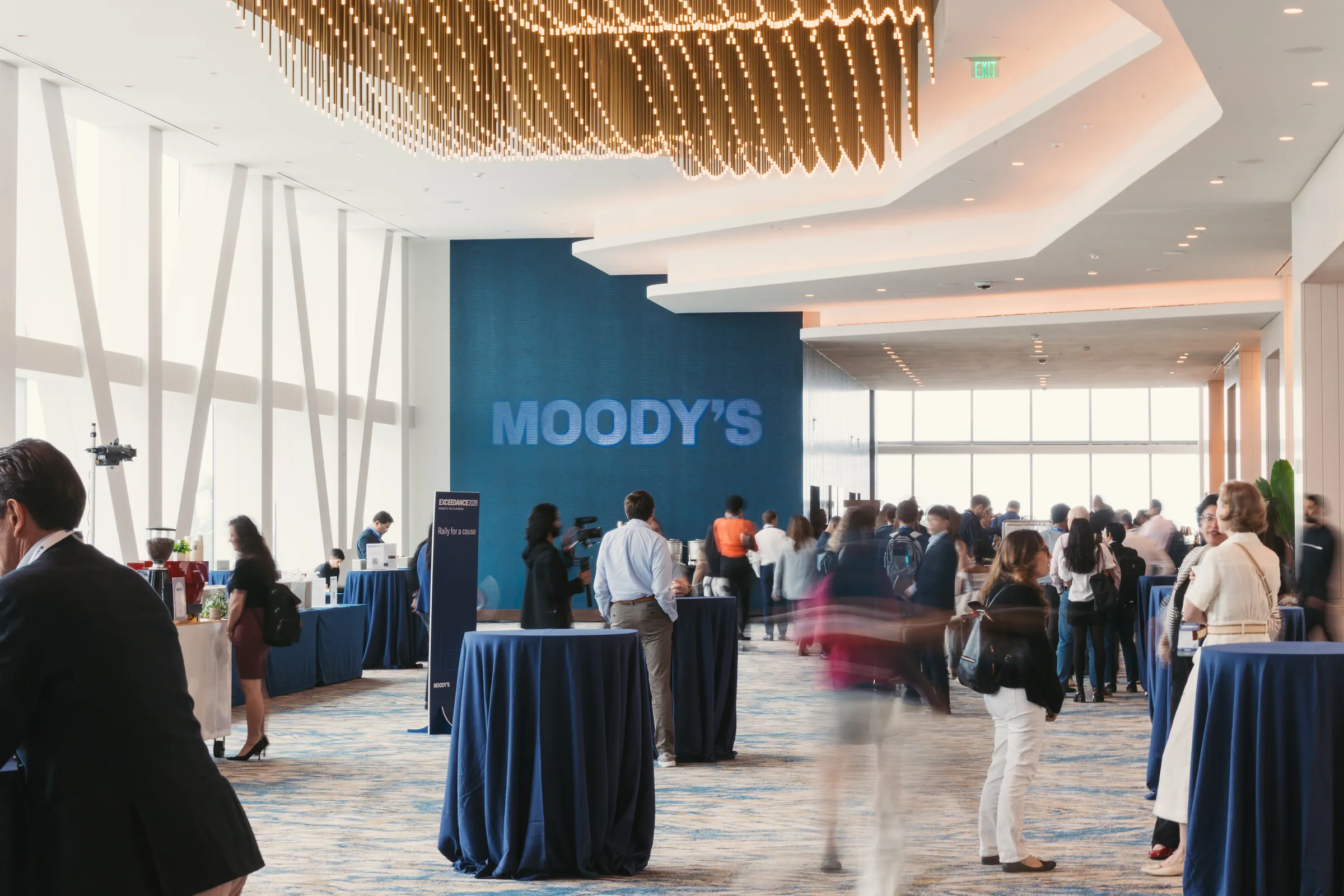 Attendees networking in the foyer beneath a large Moody’s logo wall.